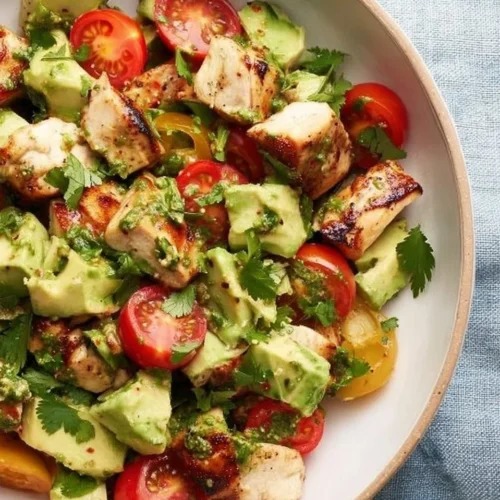 A bowl of fresh avocado chicken salad with green vegetables and dressing