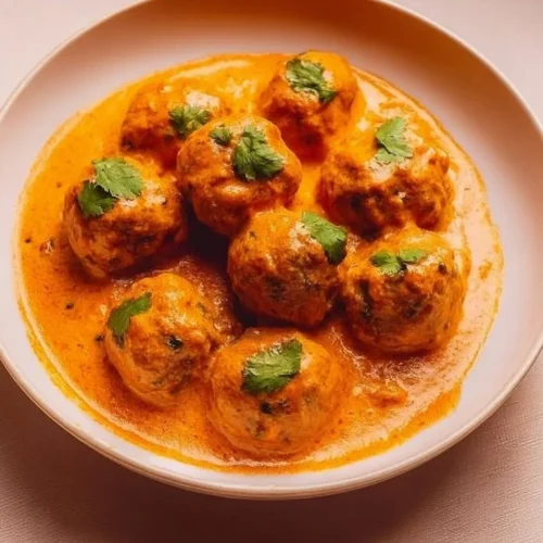 Delicious plate of Malai Kofta served with creamy sauce and garnished with fresh herbs.