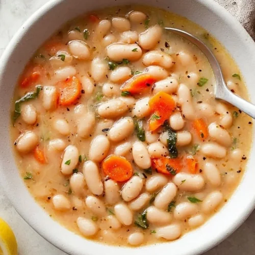 Bowl of Greek white bean soup garnished with garlic and lemon slices
