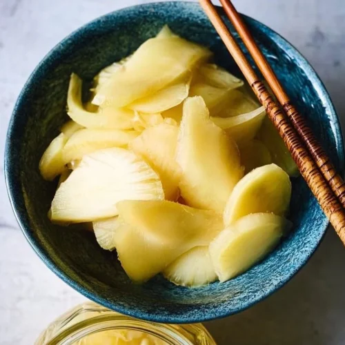 Quick pickled ginger in a glass jar with fresh ginger slices.