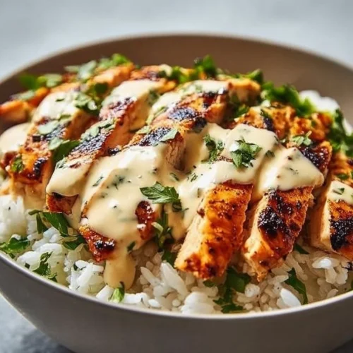 Chicken rice bowls drizzled with creamy garlic sauce served in a bowl.